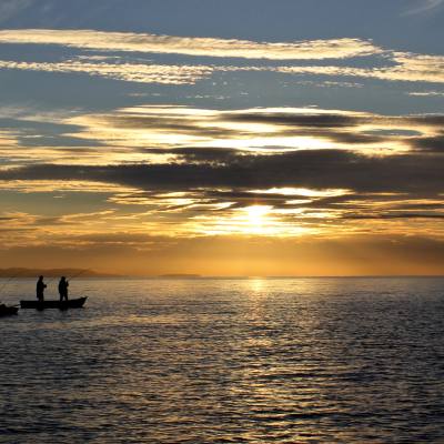 Silhouette of three people fishing from two different boats in Parksville Qualicum Beach at sunset.