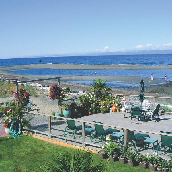Lounge chairs sit on a patio beside a beach and body of water at the Buena Vista Qualicum Beach Waterfront hotel.