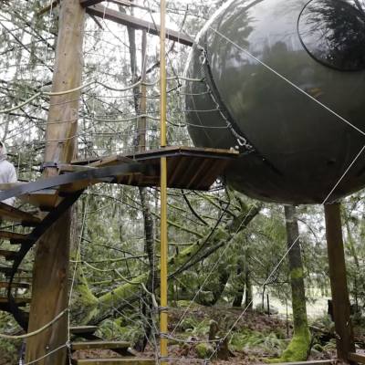 a couple climbs the stairs to a gray spherical tree house at Free Spirit Spheres in Parksville Qualicum Beach