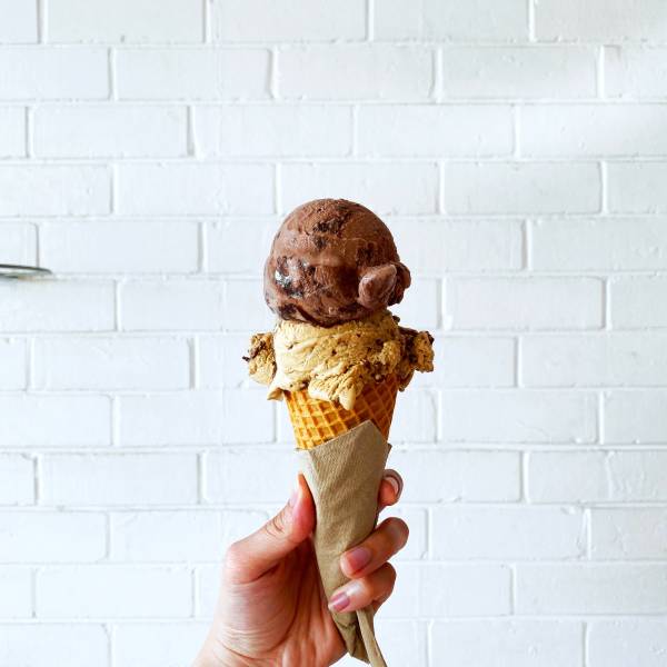 A person holding a double scoop of ice cream, featuring butter pecan and chocolate.