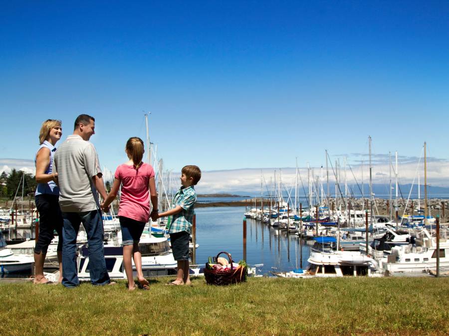 A mother, father, and two children are holding hands while standing on a grassy area overlooking Fairwinds Marina.
