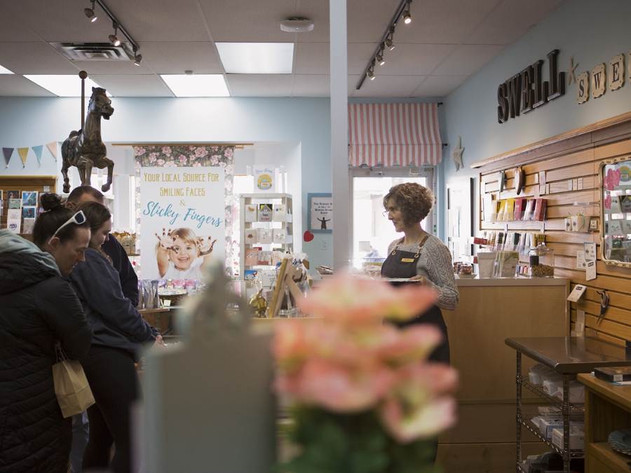 A woman smiles as she assists customers from behind a counter at Swell Sweets candy shop