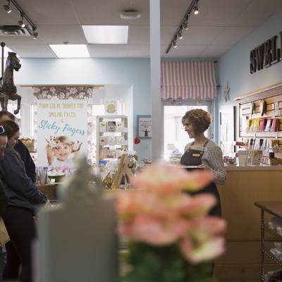 A woman smiles as she assists customers from behind a counter at Swell Sweets candy shop