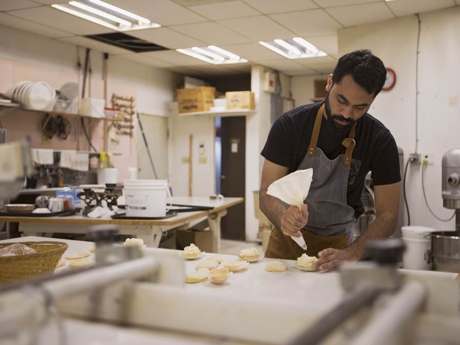 A man pipes frosting onto a baked good in a kitchen of a bakery in Qualicum Beach