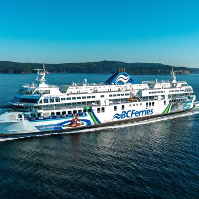 a long white, green and blue ferry with BC Ferries sails through the water to Vancouver Island