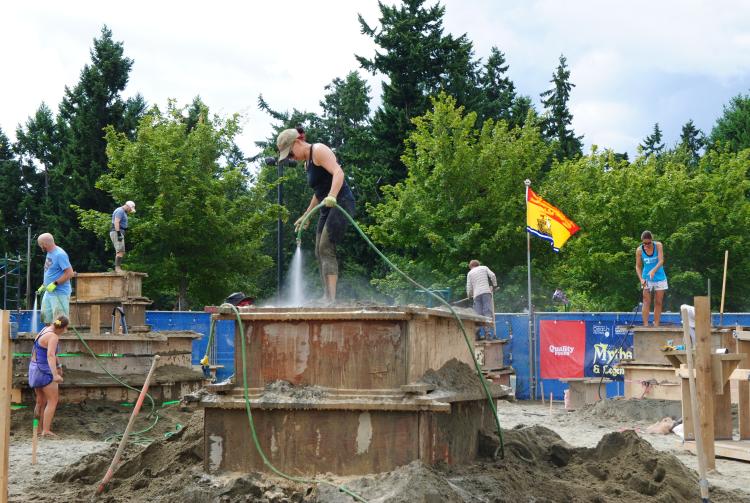 Sculptors stand atop huge blocks of sand, spraying them down with water hoses as they begin work on their sculptures.