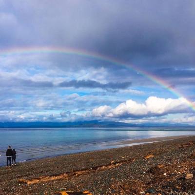a rainbow arches over the water the Beach in Parksville Qualicum Beach Photo credit: @brain.bumps