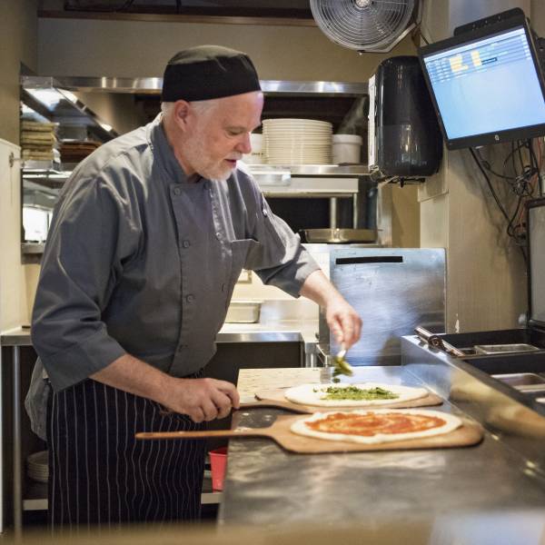 Eric Edwards, a chef wearing a gray uniform, creates two different pizzas in the kitchen at Tigh Na Mara