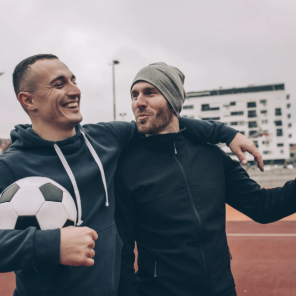 two soccer fans arm in arm holding soccer ball walking on a track