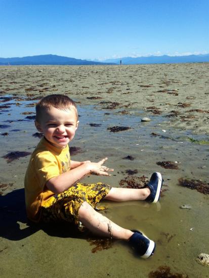 A boy sits on the sand at Rathtrevor Beach.