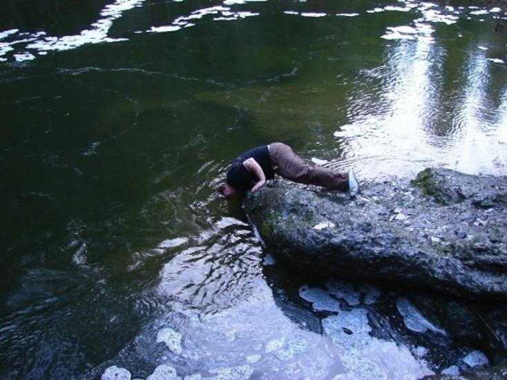 Man leaning in water to catch fish with bare hands in the Englishman river in Parksville, BC