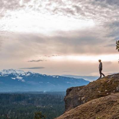 A man stands at the edge of the cliff at Little Mountain Lookout and admires mountain ranges in the distance