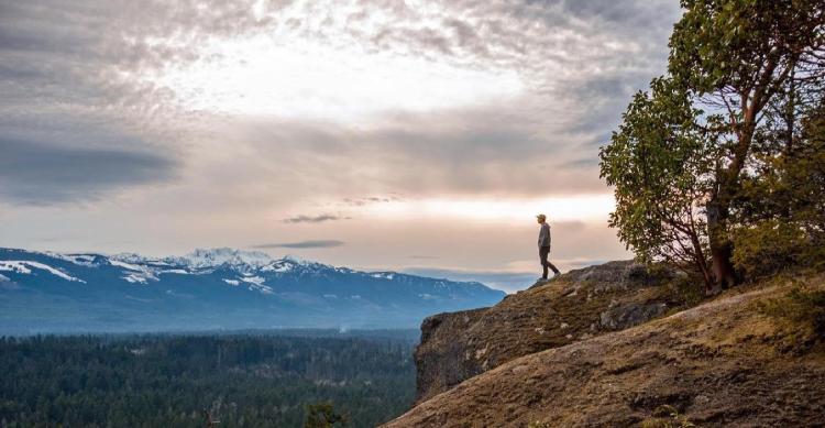 A man stands at the edge of the cliff at Little Mountain Lookout and admires mountain ranges in the distance