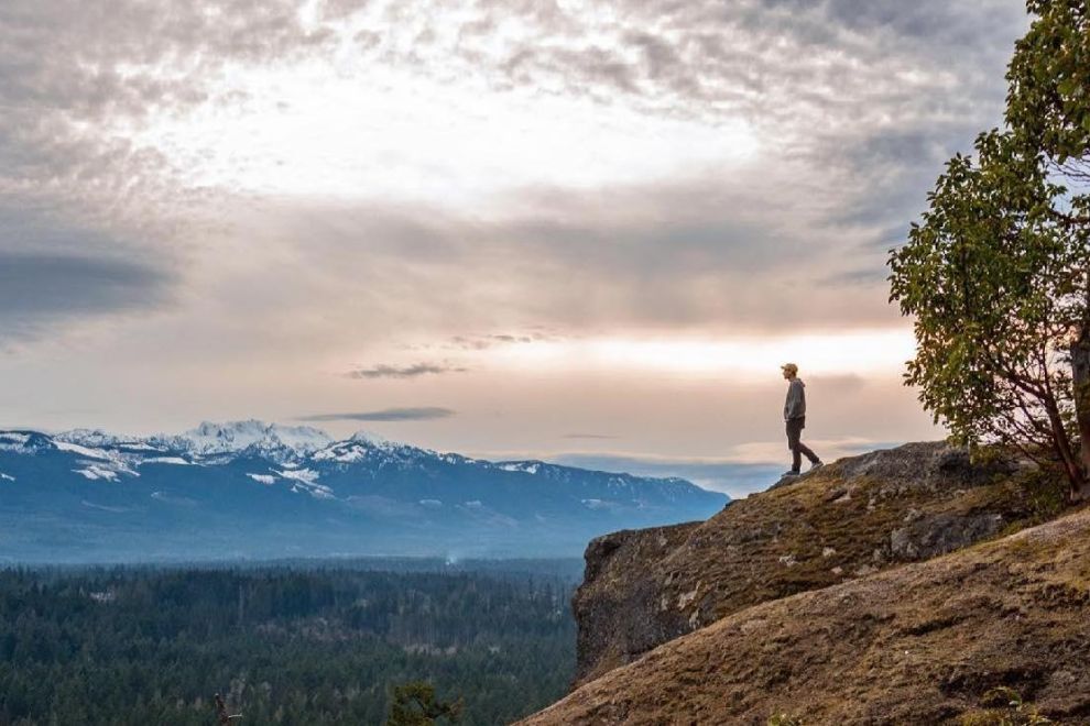 A man stands at the edge of the cliff at Little Mountain Lookout and admires mountain ranges in the distance