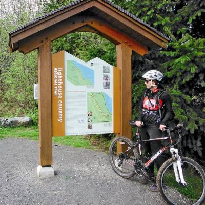 A cyclist stands with her bike by the Lighthouse trail sign.