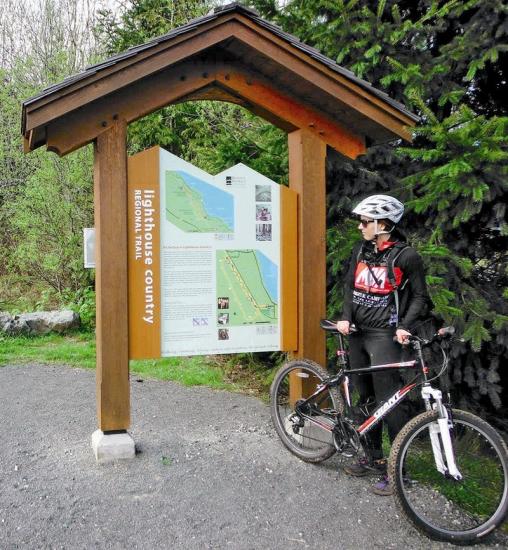 A cyclist stands with her bike by the Lighthouse trail sign.