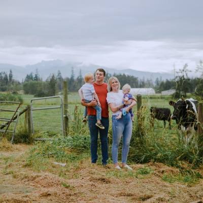 Family with two young children standing in front of cows grazing in a field at Little Qualicum Cheeseworks