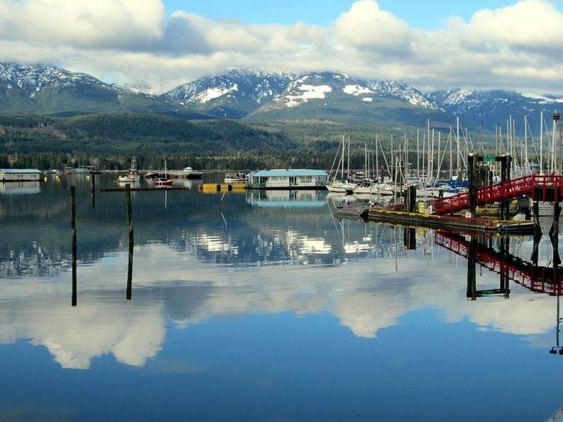 Boats in the Deep Bay Marina. Mountains and a partly cloudy sky reflect off of the water