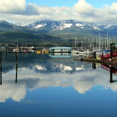 Boats in the Deep Bay Marina. Mountains and a partly cloudy sky reflect off of the water