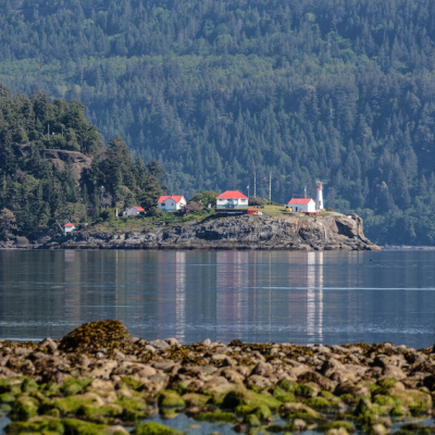 A lighthouse and a few buildings stand across the waters in the distance in Lighthouse Country.