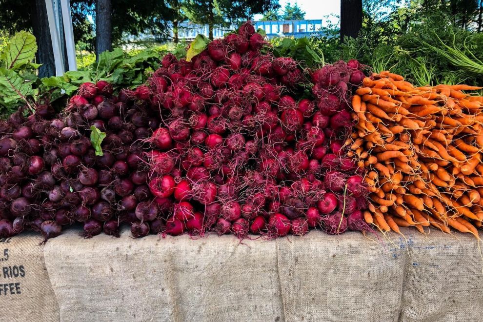 Piles of fresh radishes, beets and carrots on a table at a farmers' market in Parksville Qualicum Beach.