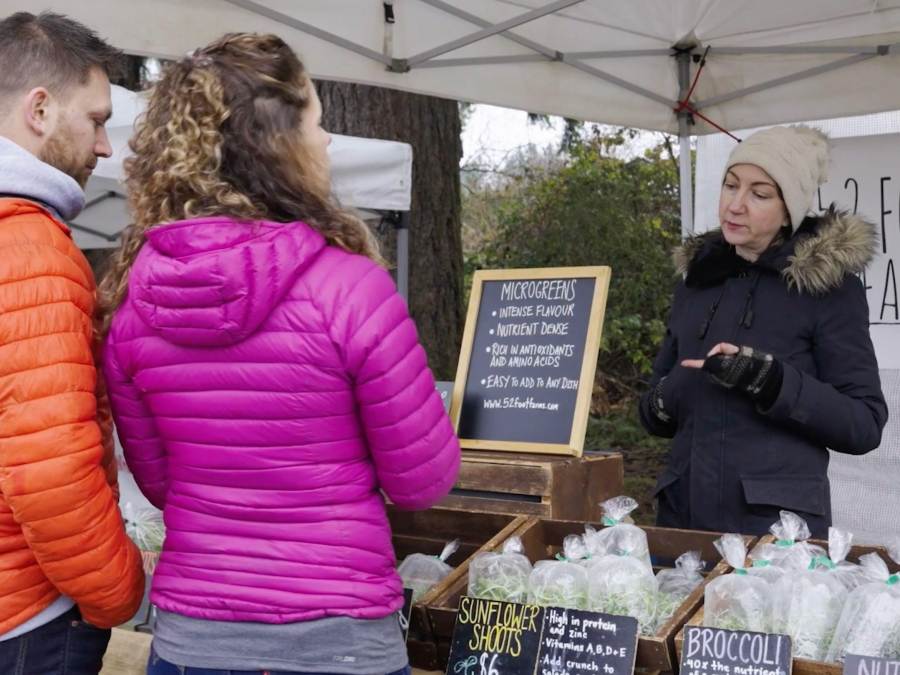 Two patrons speak with a vendor at a tented booth at the Qualicum Beach Farmers' Market.
