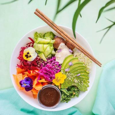 top-down view of wood chopsticks resting on a bowl of thinly sliced produce topped with pansies